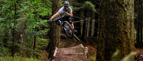 Mountainbiker springt über Hindernisrampe im Wald