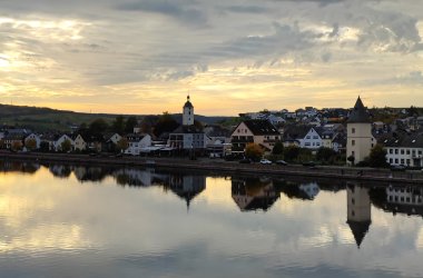 Bild zeigt Mehring im Sonnenuntergang von der Mosel aus gesehen. Häuserreihen spiegeln sich im Wasser